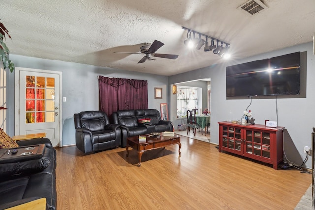 living area featuring a textured ceiling, ceiling fan, visible vents, and wood finished floors