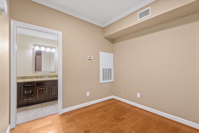 empty room with visible vents, ornamental molding, a sink, and light wood-type flooring