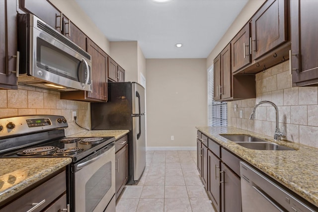 kitchen featuring dark brown cabinets, a sink, stainless steel appliances, baseboards, and backsplash