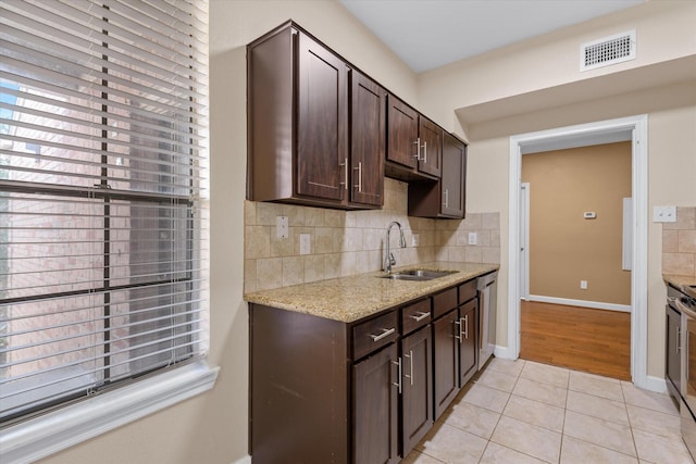 kitchen featuring dark brown cabinetry, tasteful backsplash, a sink, light tile patterned floors, and stainless steel appliances