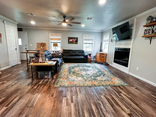living area with a ceiling fan, visible vents, a fireplace, wood finished floors, and ornamental molding