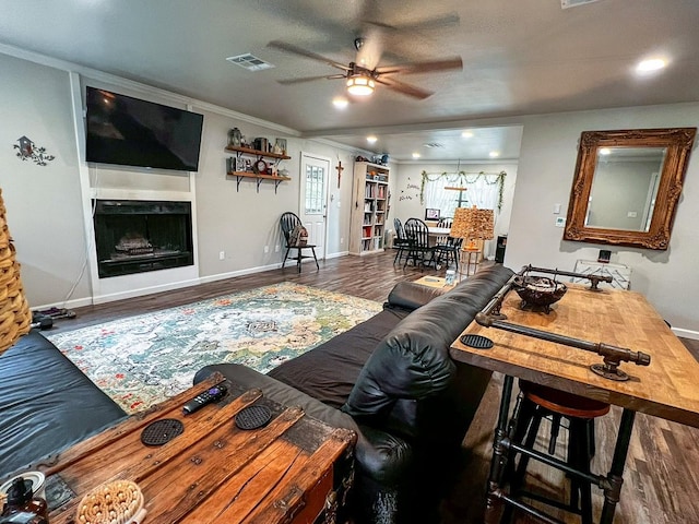 living area featuring ceiling fan, ornamental molding, wood finished floors, and visible vents
