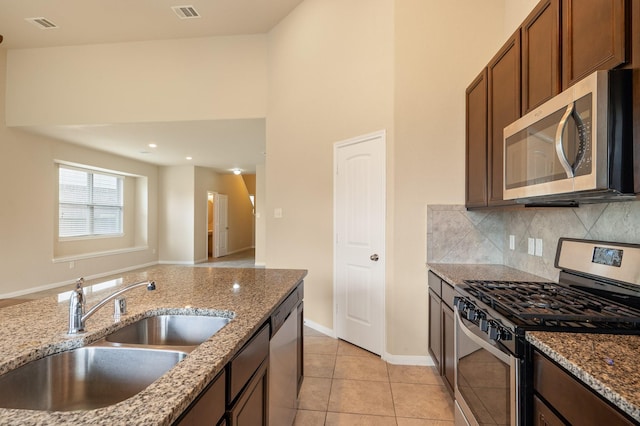 kitchen featuring light tile patterned flooring, light stone countertops, appliances with stainless steel finishes, a sink, and backsplash