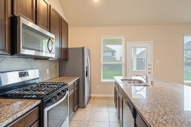 kitchen featuring decorative backsplash, dark brown cabinetry, appliances with stainless steel finishes, light stone countertops, and a sink