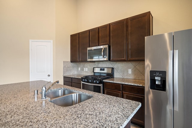 kitchen with light stone countertops, dark brown cabinets, tasteful backsplash, a sink, and stainless steel appliances