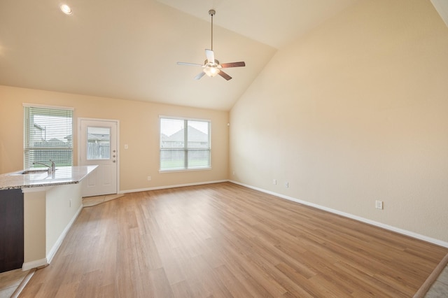 unfurnished living room featuring a sink, light wood finished floors, a ceiling fan, baseboards, and lofted ceiling