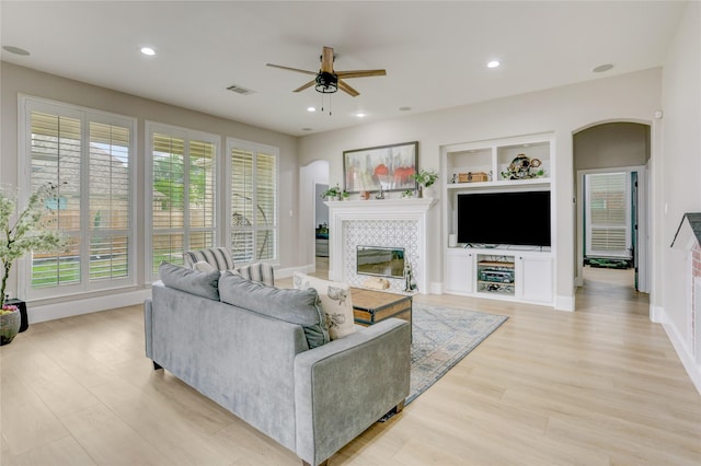 living room with light wood-style floors, arched walkways, a ceiling fan, a tile fireplace, and visible vents