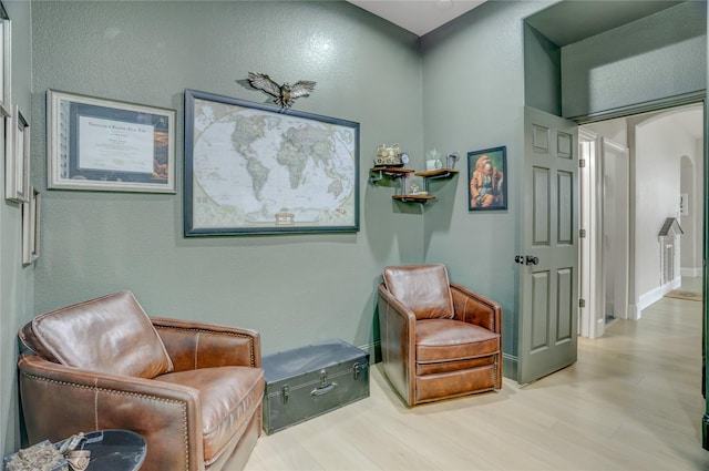 living area with arched walkways, a textured wall, and wood finished floors
