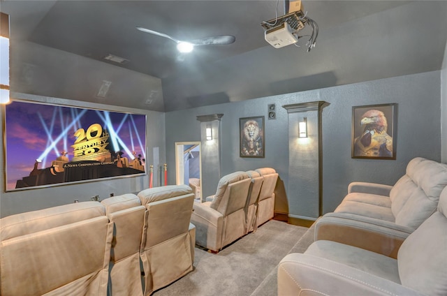 carpeted cinema room with a textured wall, vaulted ceiling, and visible vents