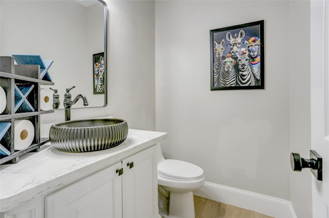 bathroom featuring baseboards, wood finished floors, toilet, and vanity