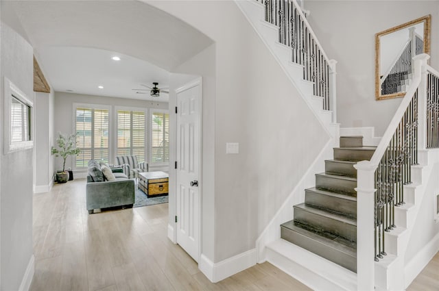 staircase featuring baseboards, ceiling fan, arched walkways, and wood finished floors