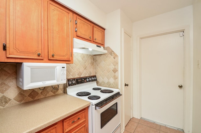 kitchen with tasteful backsplash, light countertops, light tile patterned floors, under cabinet range hood, and white appliances