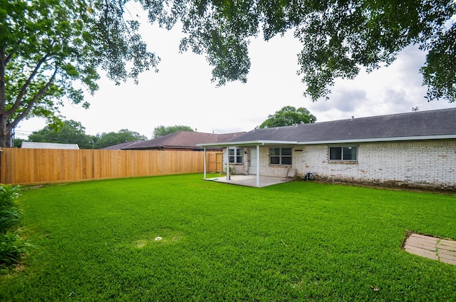 rear view of property with a patio, a fenced backyard, a yard, and brick siding