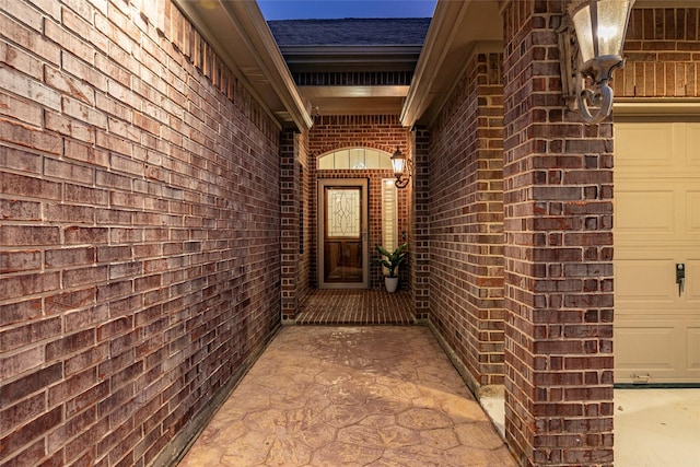 view of exterior entry with brick siding, a shingled roof, and a garage