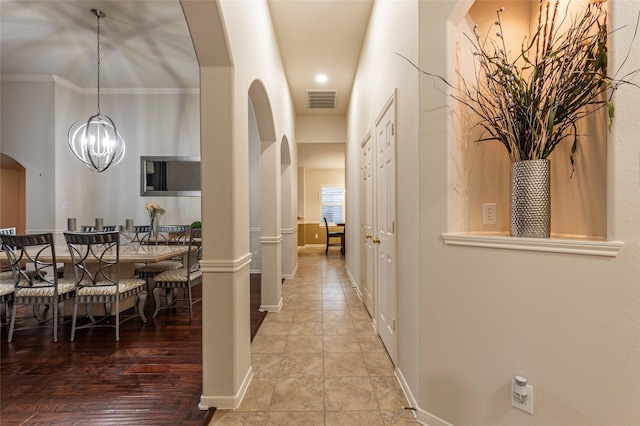 corridor featuring arched walkways, a notable chandelier, visible vents, and baseboards