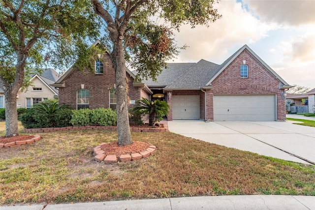 traditional-style home with driveway, a front yard, roof with shingles, brick siding, and an attached garage