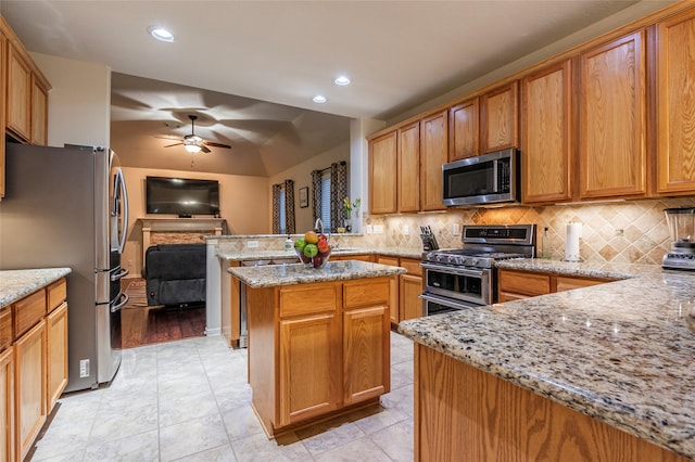 kitchen with ceiling fan, appliances with stainless steel finishes, tasteful backsplash, light stone counters, and a peninsula