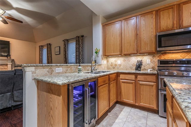 kitchen featuring ceiling fan, appliances with stainless steel finishes, a sink, light stone counters, and beverage cooler