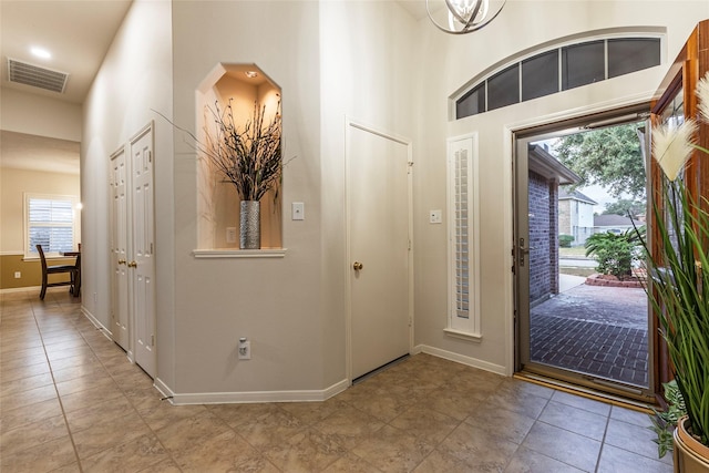 foyer entrance featuring baseboards, tile patterned floors, a towering ceiling, and visible vents