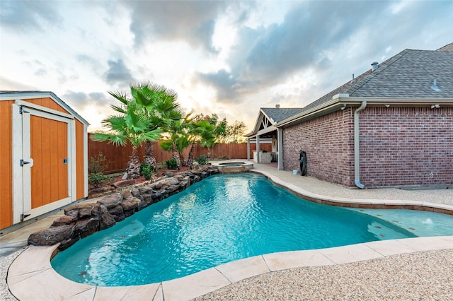 view of pool with a pool with connected hot tub, an outdoor structure, a shed, a fenced backyard, and a patio