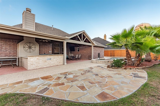 back of property with an in ground hot tub, a ceiling fan, a chimney, a patio area, and brick siding
