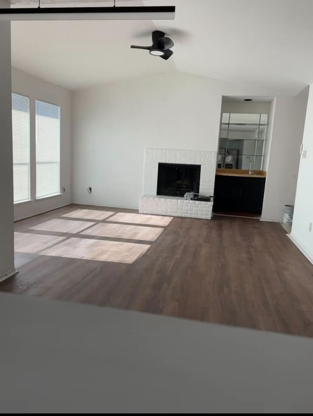 unfurnished living room featuring ceiling fan, a fireplace, baseboards, wood finished floors, and lofted ceiling