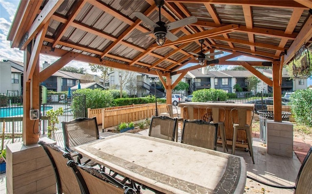 view of patio featuring ceiling fan, fence, outdoor dry bar, and a residential view