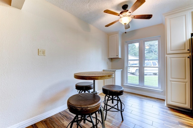 dining room featuring a textured wall, light wood-style floors, a textured ceiling, a ceiling fan, and baseboards