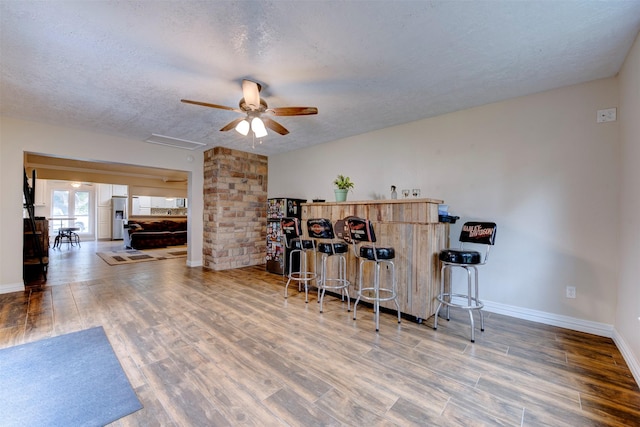 bar featuring baseboards, a ceiling fan, a textured ceiling, and wood finished floors