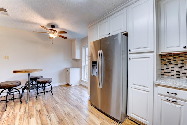 kitchen with backsplash, stainless steel refrigerator with ice dispenser, a textured ceiling, and visible vents