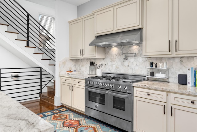 kitchen with backsplash, double oven range, cream cabinets, under cabinet range hood, and dark wood-type flooring