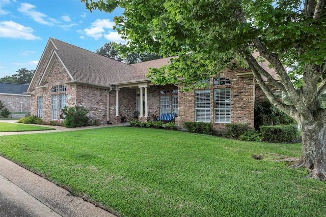 view of front of home featuring brick siding, a front yard, and roof with shingles