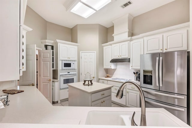 kitchen with backsplash, visible vents, under cabinet range hood, white appliances, and white cabinetry