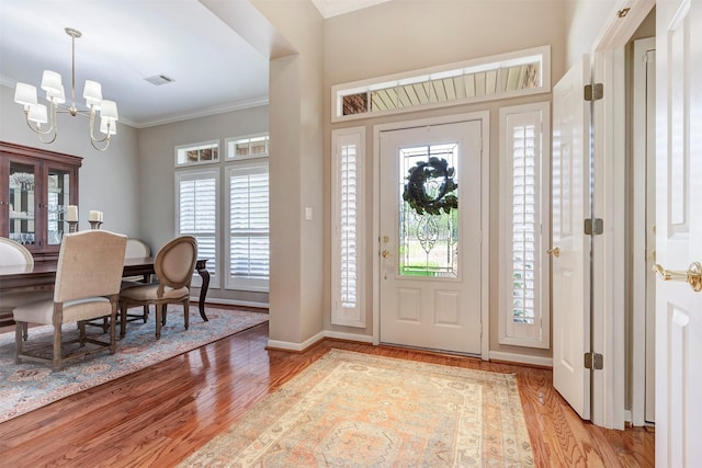 foyer entrance featuring visible vents, ornamental molding, baseboards, light wood-style flooring, and a notable chandelier