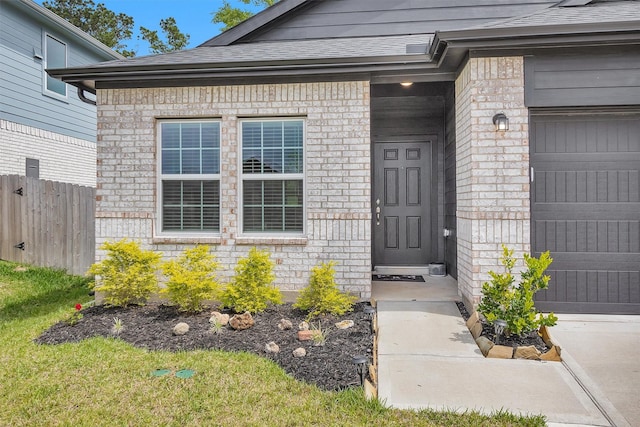 entrance to property with brick siding, fence, roof with shingles, and a garage