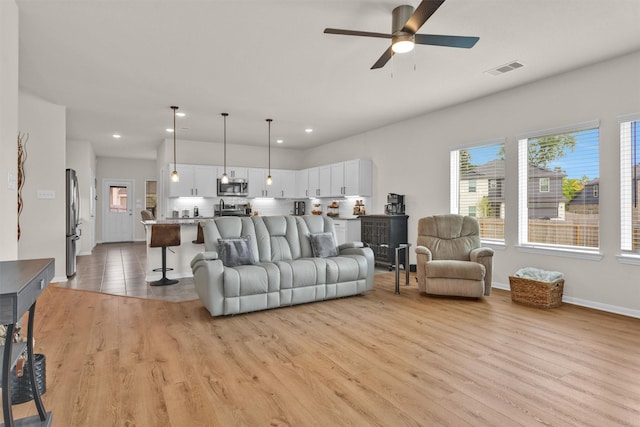 living room with light wood finished floors, a ceiling fan, baseboards, recessed lighting, and visible vents