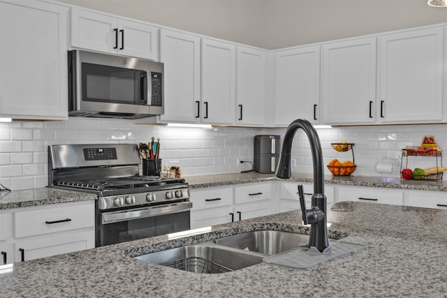 kitchen with light stone counters, a sink, white cabinetry, and stainless steel appliances