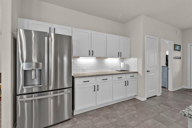 kitchen with decorative backsplash, light stone countertops, stainless steel fridge with ice dispenser, baseboards, and white cabinets