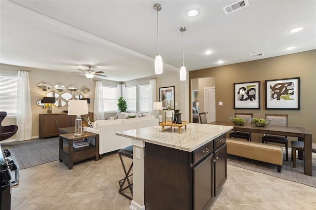 kitchen with ceiling fan, a kitchen breakfast bar, open floor plan, a kitchen island, and visible vents