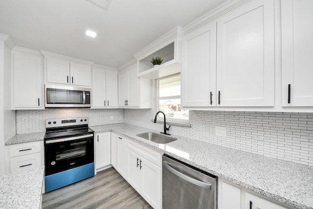 kitchen with decorative backsplash, white cabinets, a sink, light wood finished floors, and stainless steel appliances
