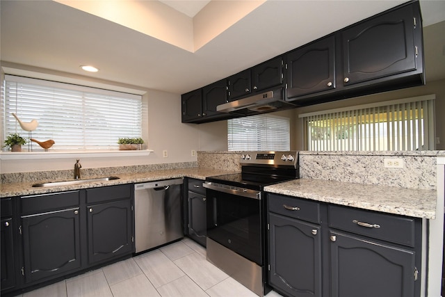 kitchen with light countertops, under cabinet range hood, a sink, light tile patterned floors, and stainless steel appliances