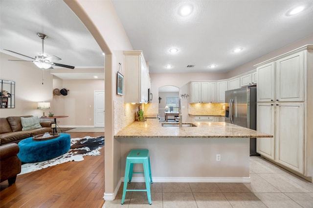 kitchen featuring light stone counters, arched walkways, a peninsula, open floor plan, and stainless steel refrigerator with ice dispenser