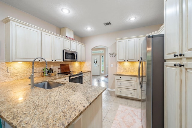 kitchen with backsplash, arched walkways, a sink, light stone counters, and stainless steel appliances