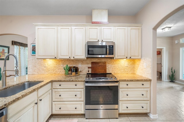 kitchen featuring arched walkways, a sink, light tile patterned floors, light stone counters, and stainless steel appliances