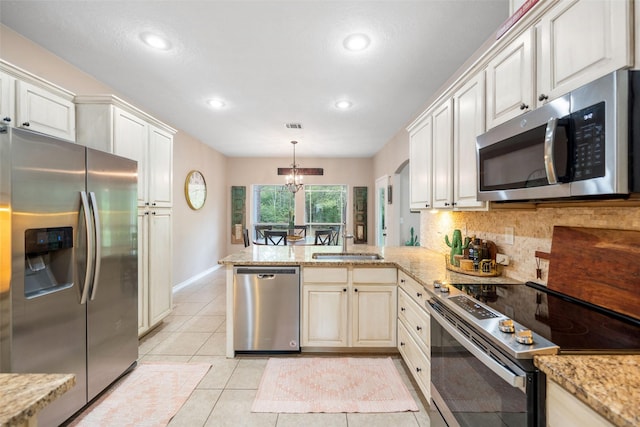 kitchen featuring a peninsula, a chandelier, a sink, appliances with stainless steel finishes, and backsplash