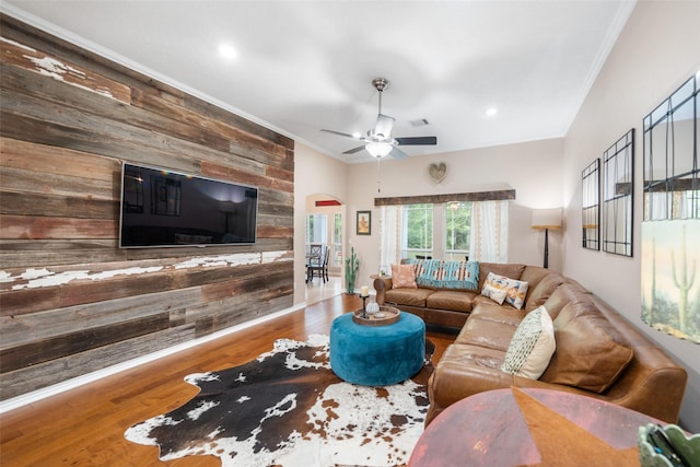 living area featuring a ceiling fan, arched walkways, wood finished floors, wooden walls, and ornamental molding