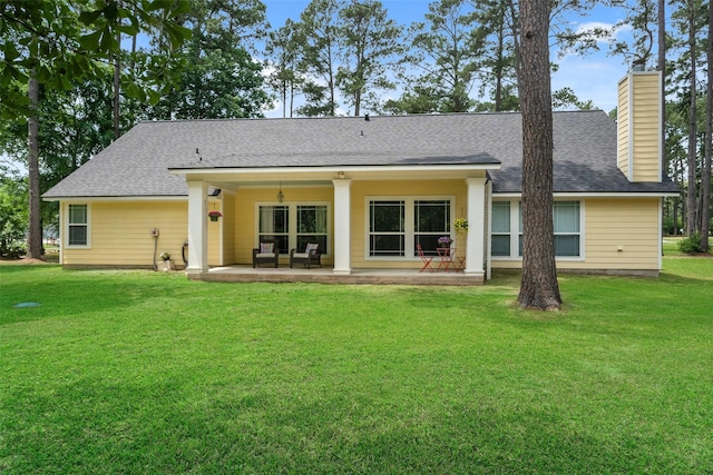 back of property with a lawn, a patio, a chimney, and roof with shingles