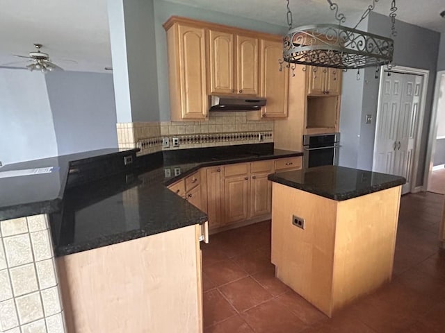 kitchen featuring light brown cabinetry, under cabinet range hood, a ceiling fan, and stainless steel oven