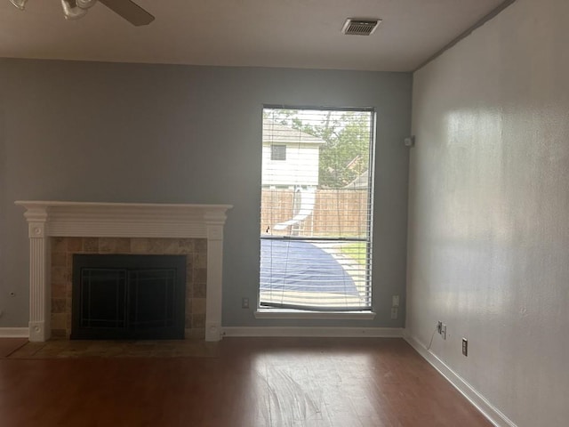 unfurnished living room with a ceiling fan, baseboards, wood finished floors, a tile fireplace, and visible vents