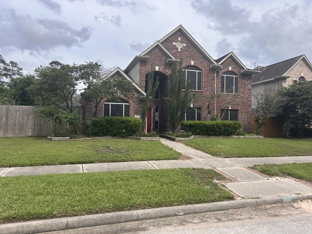 traditional-style home featuring fence, a front yard, and brick siding